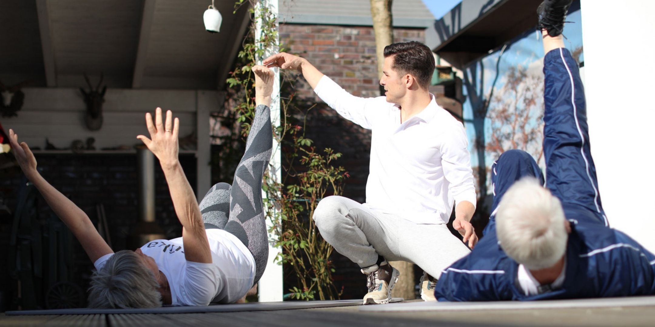 Zwei liegende Patienten machen mit Michel Menzel Präventionsübungen und Physiotherapie