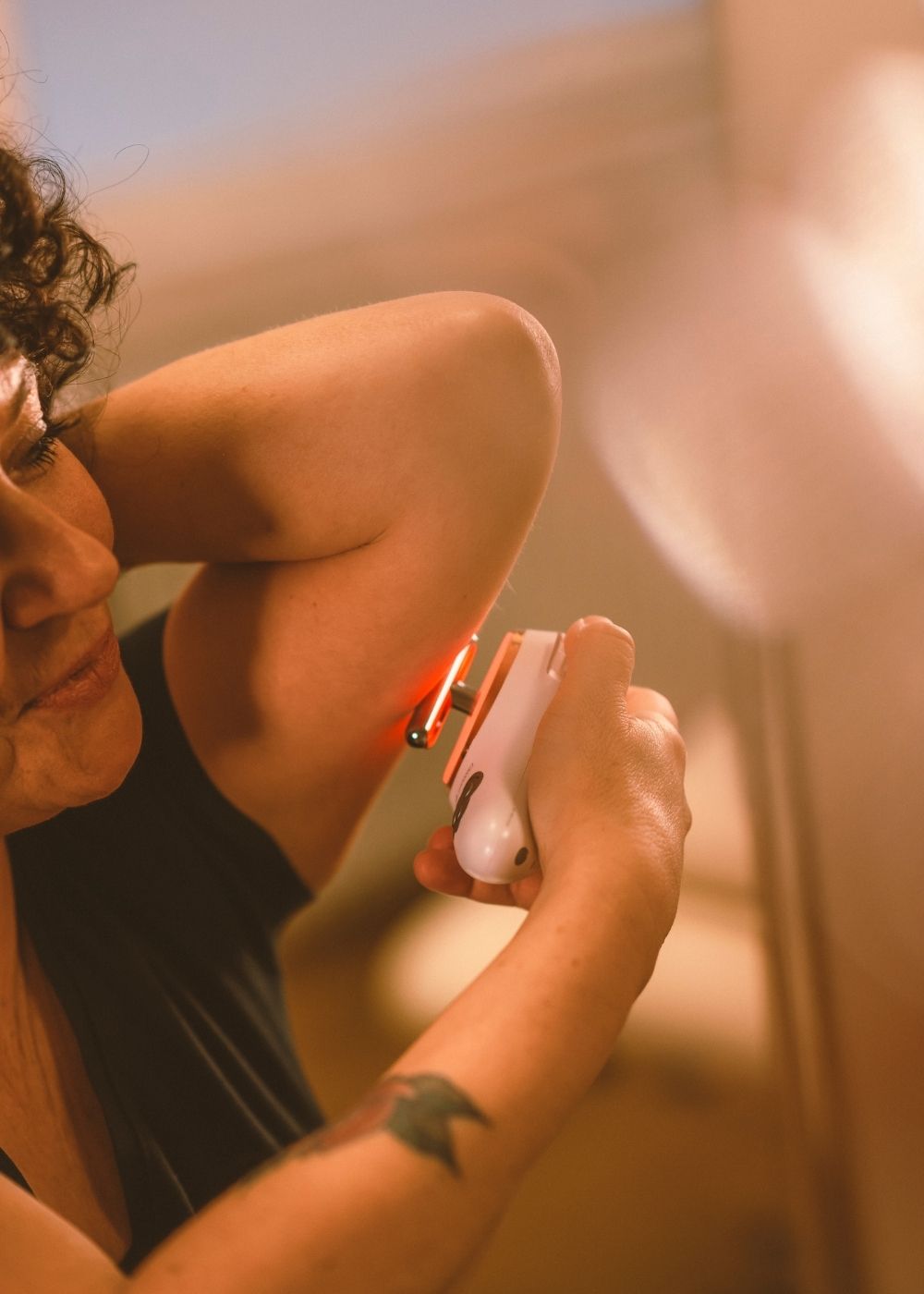 Frau hält sich Evosonics SoundWave Personal an den Oberarm um eine Lymphdrainage gegen schlaffe Oberarme mit Schallvibrationen und Rotlicht  durchzuführen. | Therapiegold